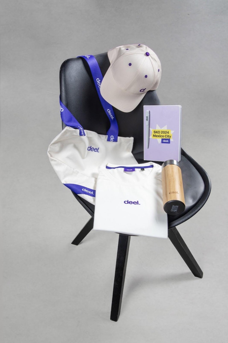 Kit de onboarding de marca Deel con gorra, lanyard, tote y camiseta sobre silla